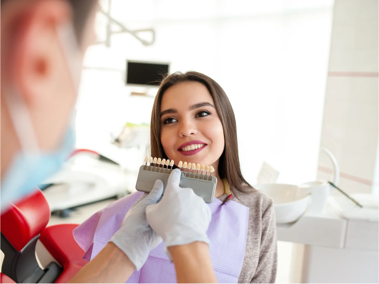 Smiling woman holding mirror examining her teeth in dental office