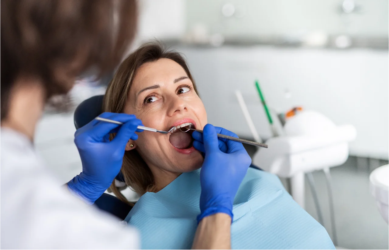 Woman in dental chair receiving examination from dentist wearing blue gloves with dental equipment visible