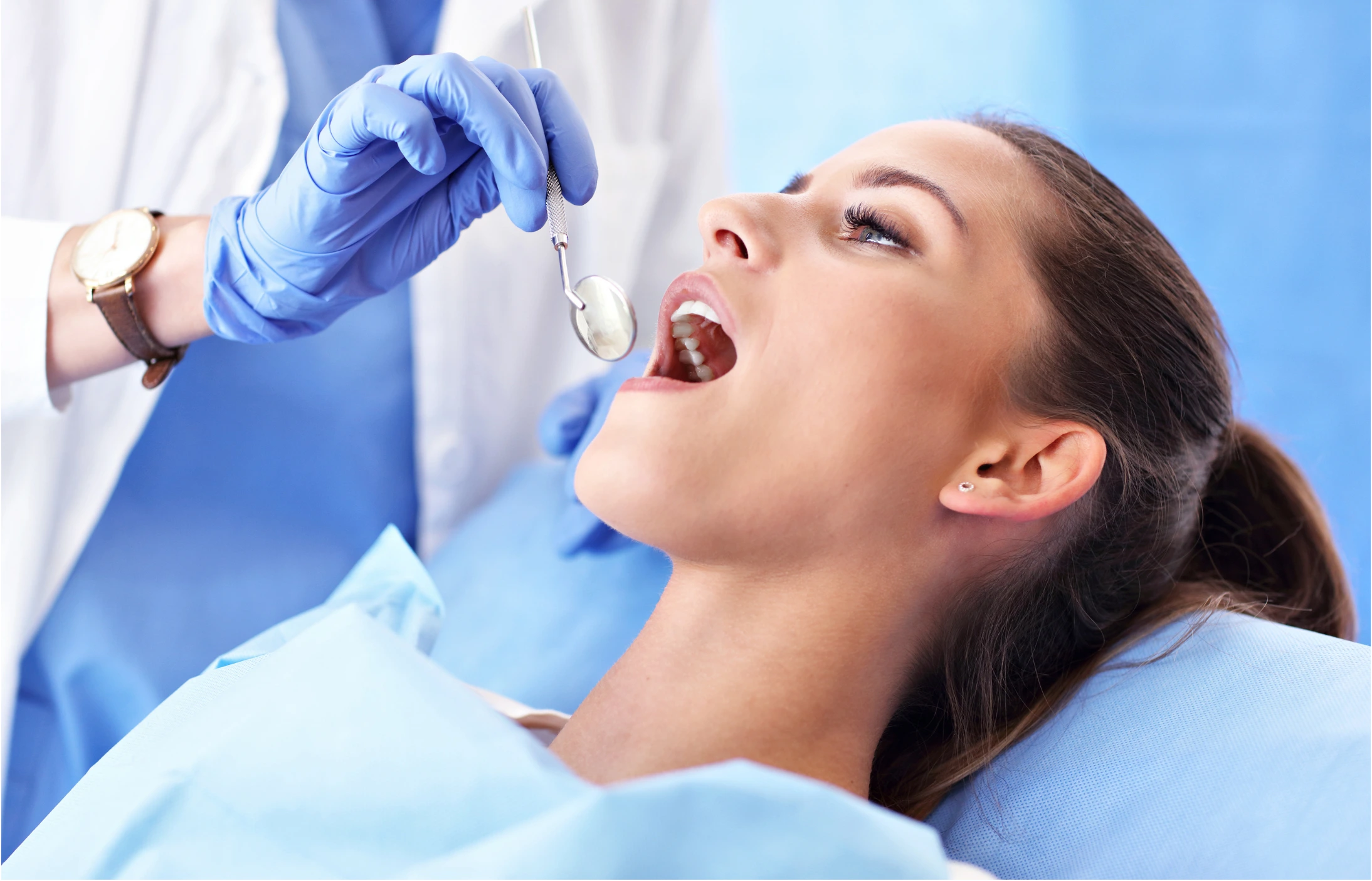 Woman in dental chair with mouth open receiving dental treatment from dentist wearing blue gloves