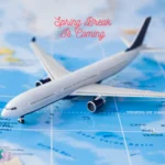 A toy airplane resting on a world map with "Spring Break Is Coming" text, representing travel plans for Tacoma and JBLM families.